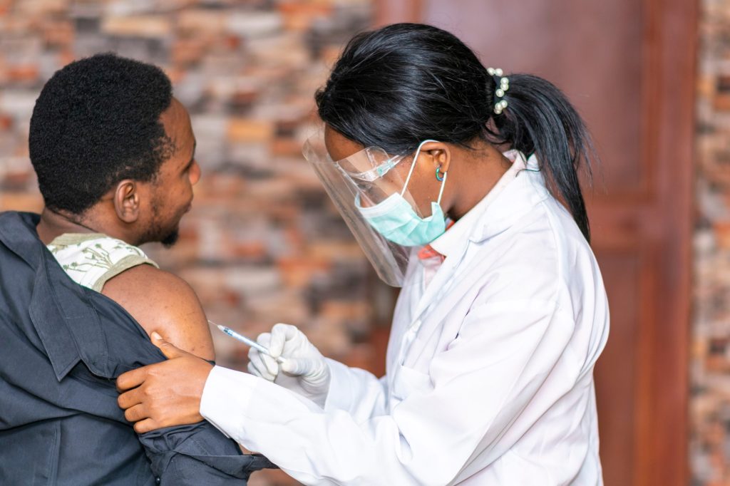 Health worker in a face shield vaccinating a man