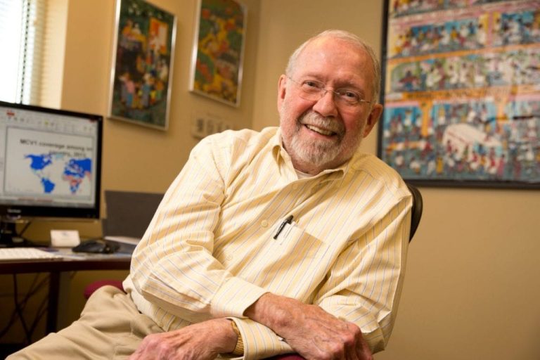 Public health leader seated in an office, smiling, with global health maps and artwork displayed in the background