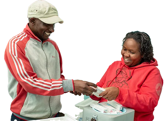 Two smiling health workers exchanging vaccine supplies beside a vaccine cold box