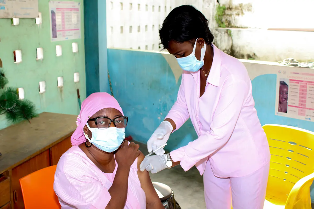 Health worker in pink scrubs vaccinating a woman wearing a face mask