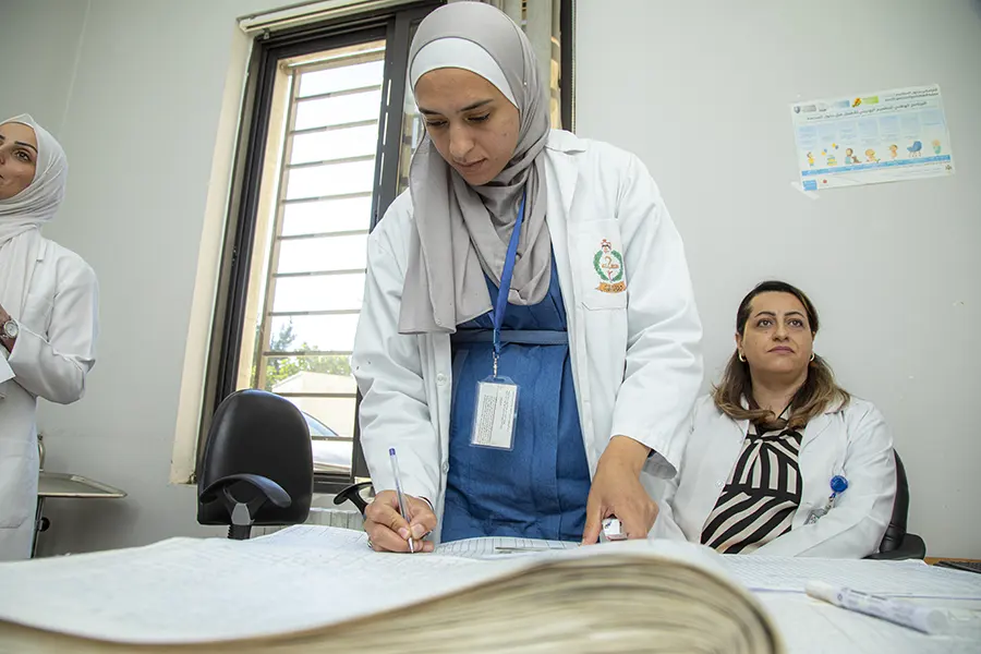 Health workers in white coats reviewing records at a clinic desk