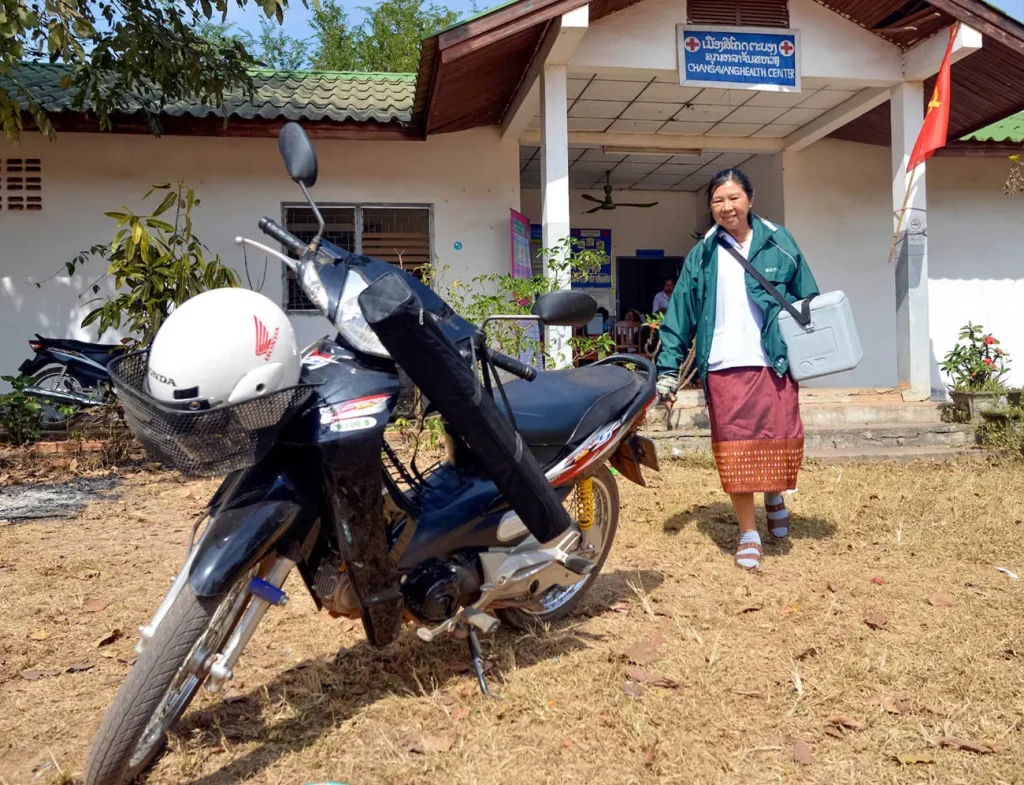Health worker walking out of a rural health center in Lao PDR, with a motorbike parked in front