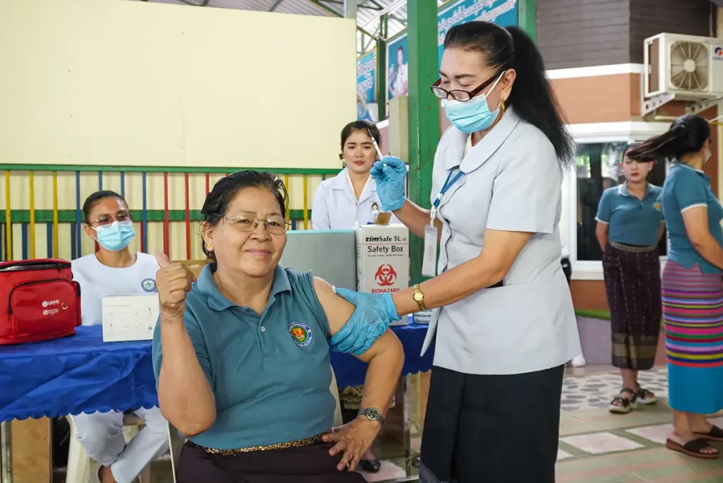 Smiling woman receiving a vaccine while others wait at a vaccination site