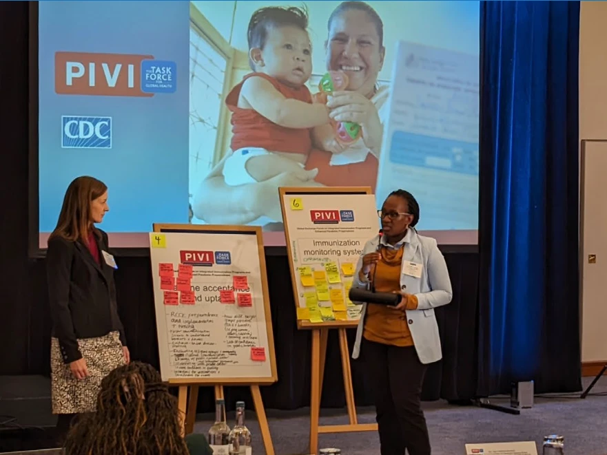 Speakers presenting at a PIVI and CDC workshop, with a slide and poster boards on stage