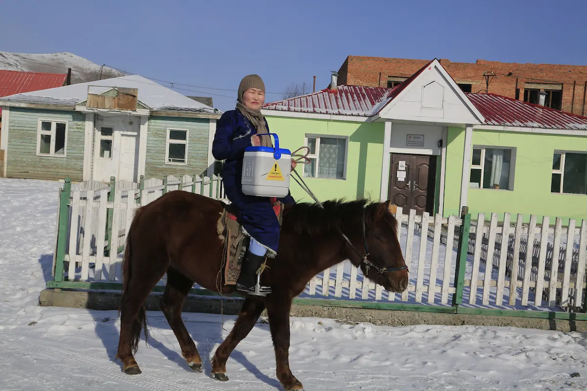 Health worker on horseback carrying a vaccine cooler in rural Mongolia