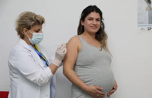 Health worker in a face mask vaccinating a pregnant woman